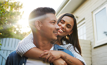 A young adult couple embraces outside their home.