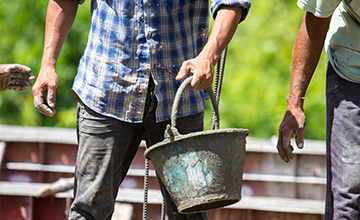 Man holding a cement covered bucket on a construction site.