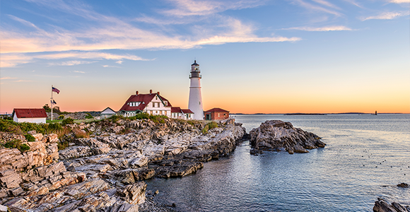 A view of a lighthouse and buildings on the coast of New England.