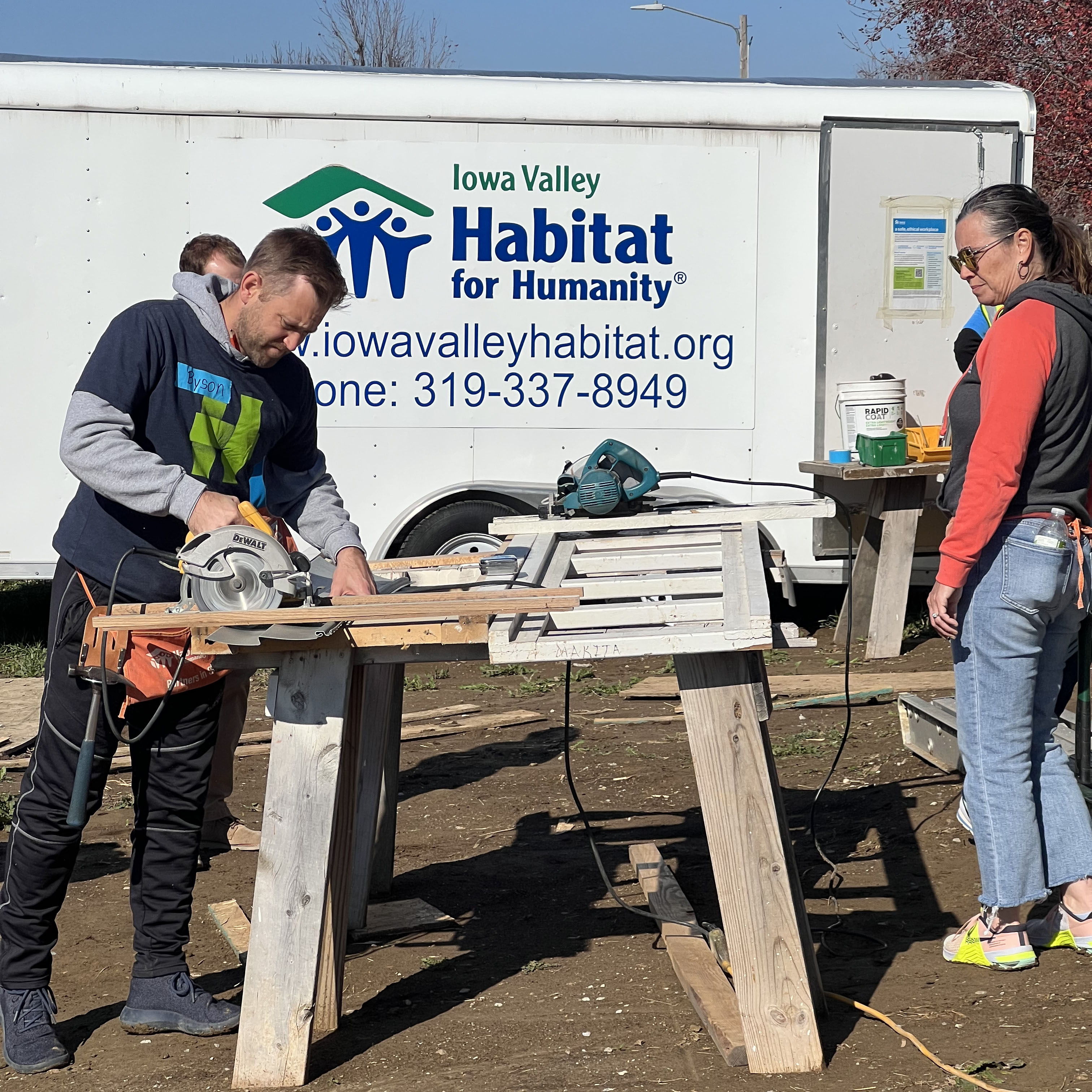 Hills Bank employee cutting wood in front of a Habitat for Humanity trailer.