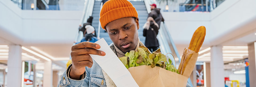 Man looking at receipt with groceries in hand