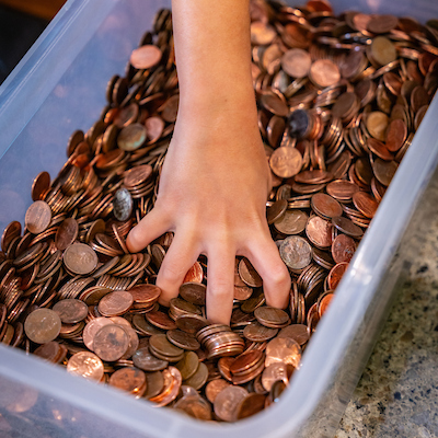 A hand grabbing from bin of pennies.