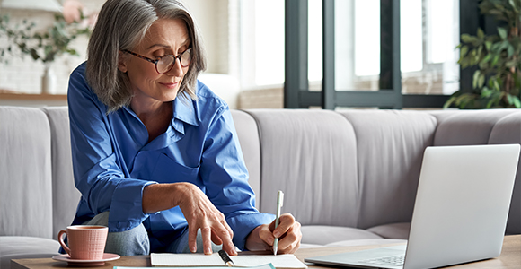 woman looking at laptop taking notes