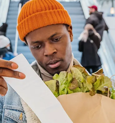 Man looking at receipt with groceries in hand