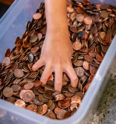 A hand grabbing from bin of pennies.