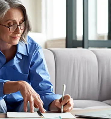 woman looking at laptop taking notes